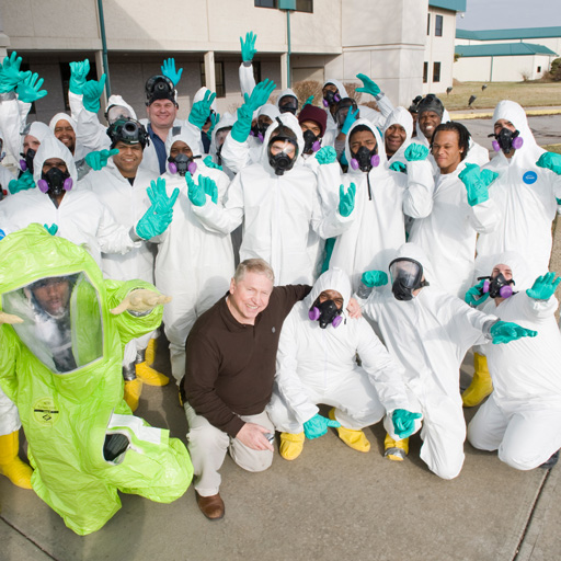 Group of students wearing protective suits, respirators and safety gear gather outdoors during hazardous materials response training.