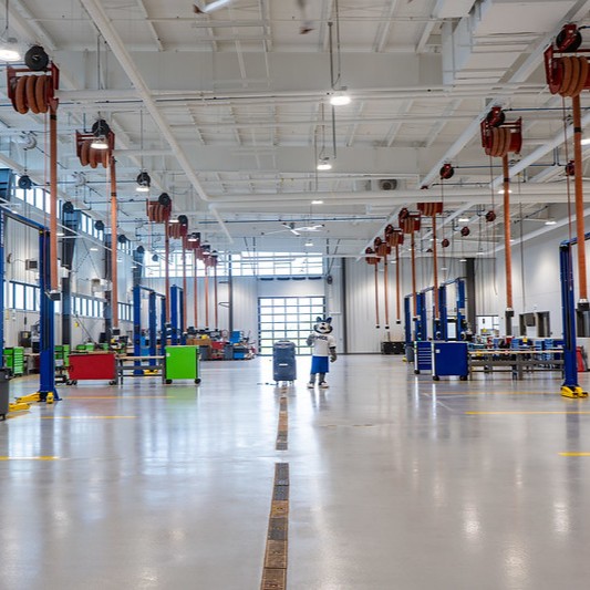 Spacious automotive training lab features vehicle lifts, tool stations and the MCC Wolf mascot standing in the center aisle.